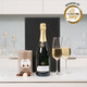 Champagne & Chocolates: A bottle of champagne is displayed alongside two filled champagne flutes and a box of chocolates. The items are arranged on a white countertop, with a sleek black box in the background. Champagne & Chocolates: A bottle of champagne is displayed alongside two filled champagne flutes and a box of chocolates. The items are arranged on a white countertop, with a sleek black box in the background.